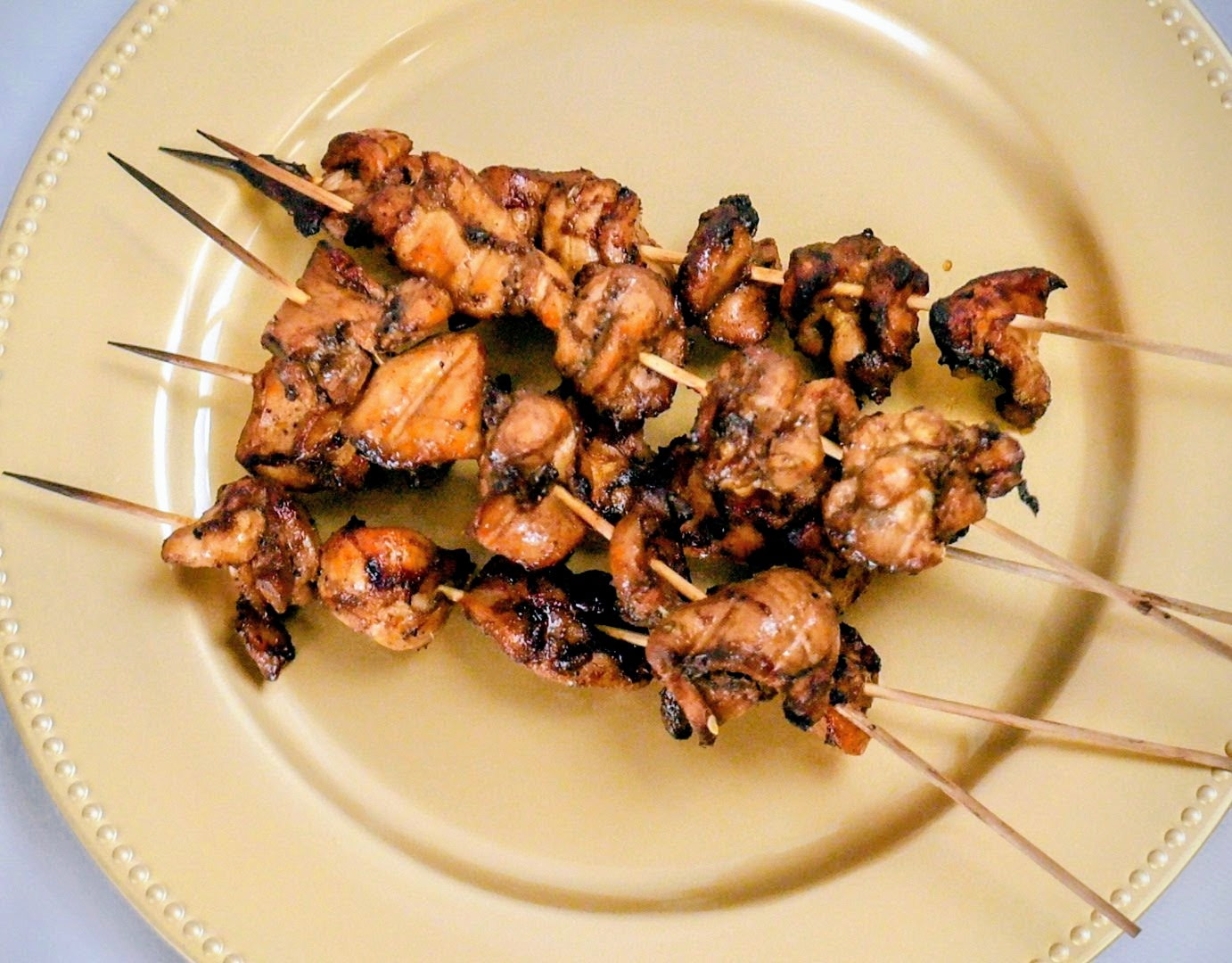 Skewers of grilled meat on a beige plate, with visible char marks and cooked texture.