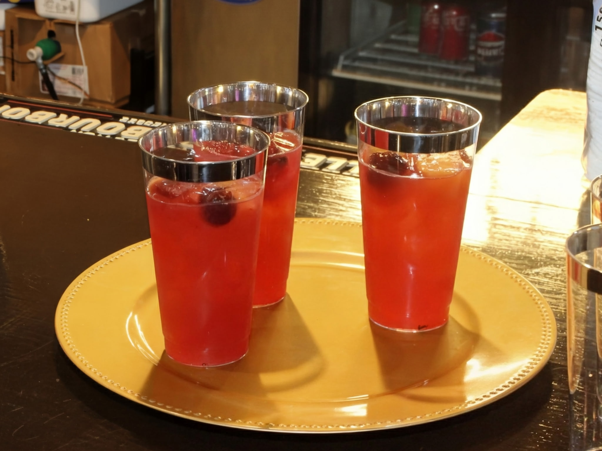 Three glasses of red beverage with berries on a gold tray on a bar counter.