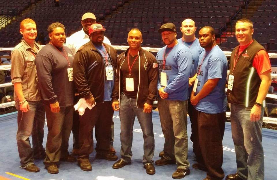 Group of ten people standing together in an indoor arena, some wearing lanyards and casual clothing.