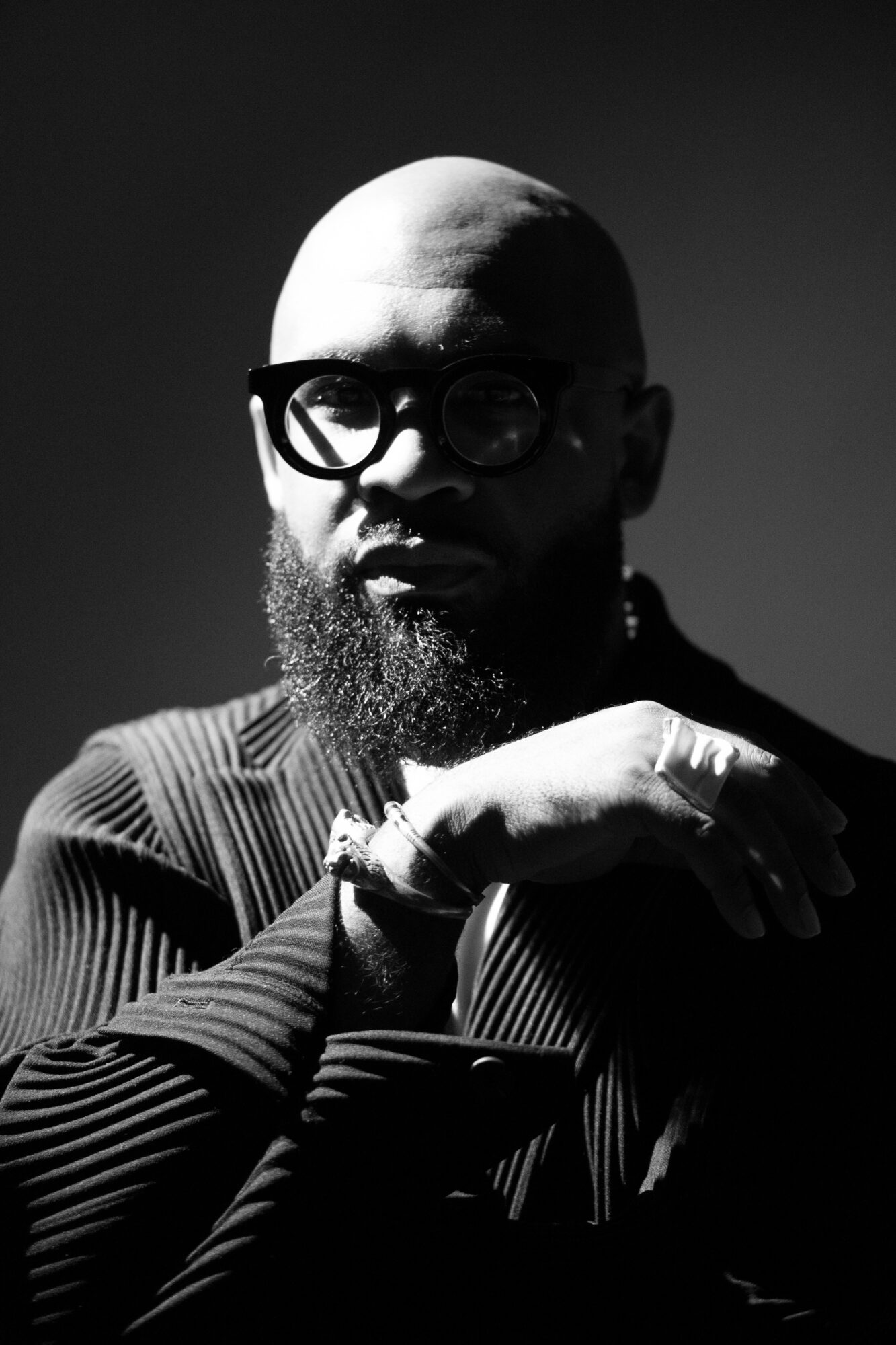 Bald man with glasses and beard, wearing a striped shirt, resting his chin on his hand, in black and white.