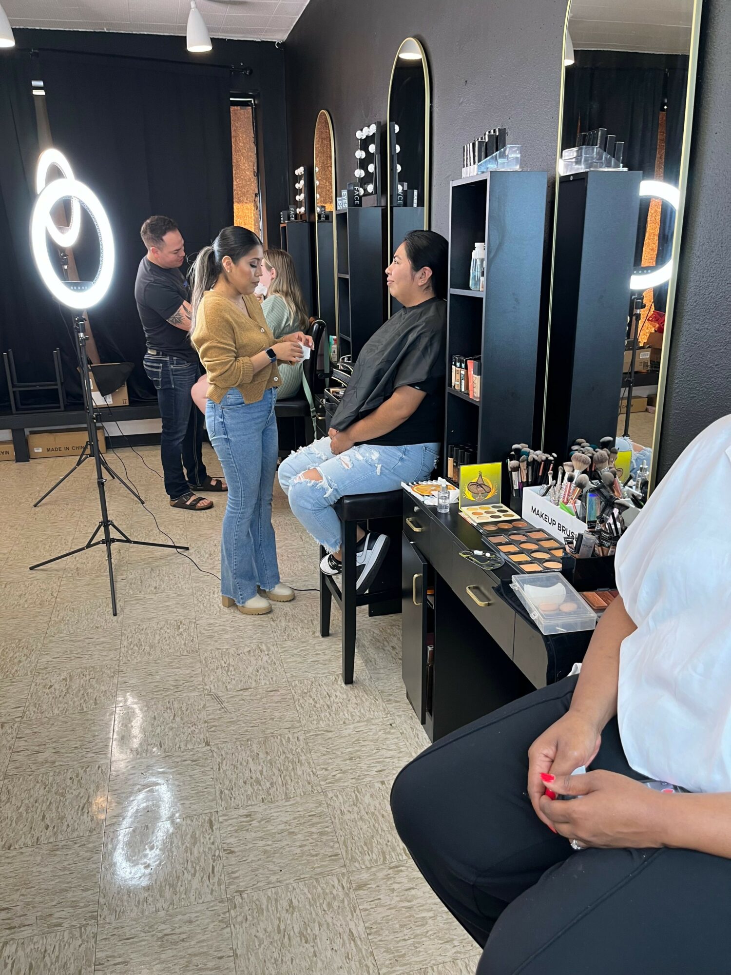 People standing and talking in a room with black walls and bright lighting, with a table and various items on it.