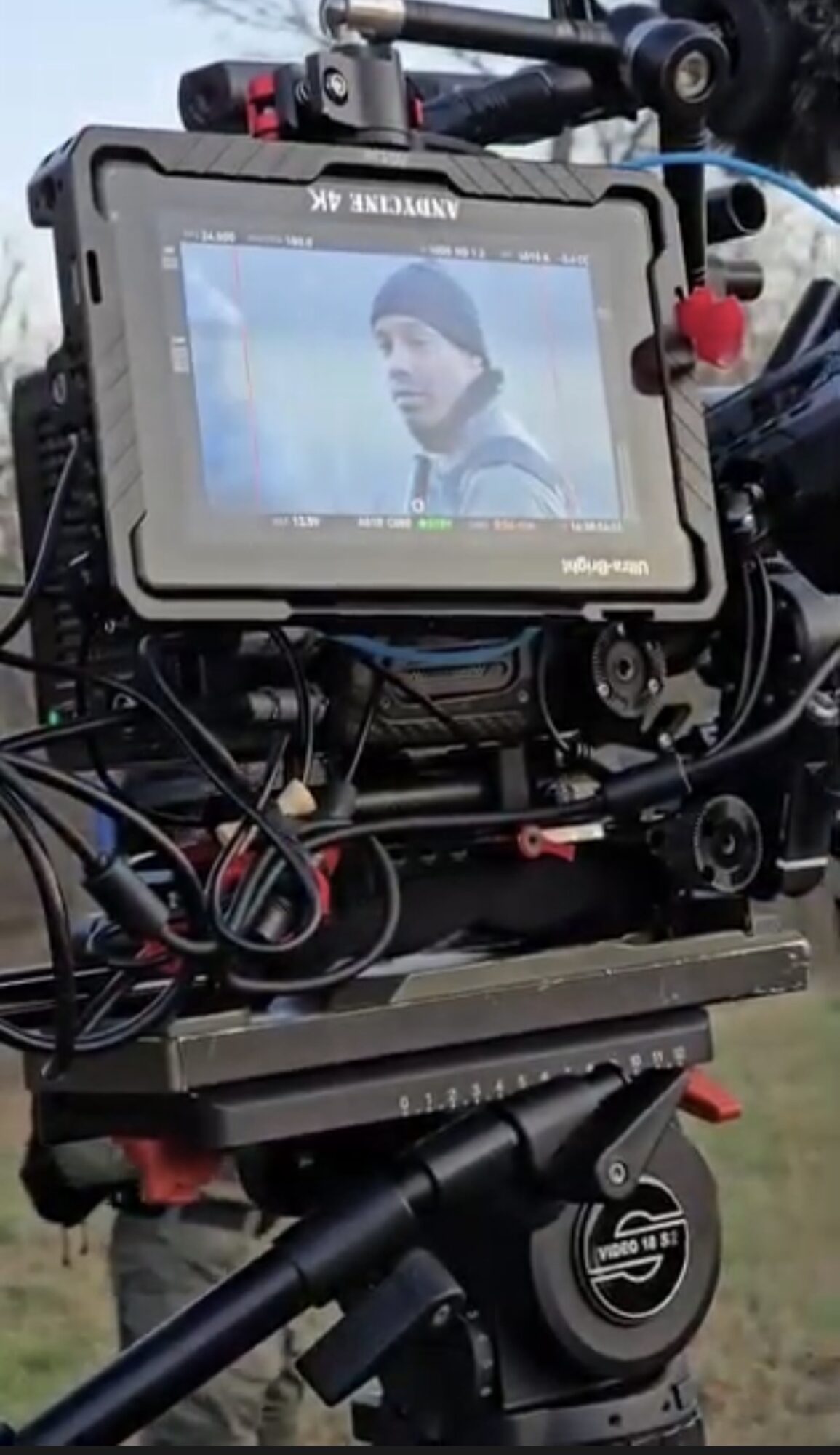 Camera monitor showing a person wearing a beanie, outdoors, with equipment and wires visible around the camera.