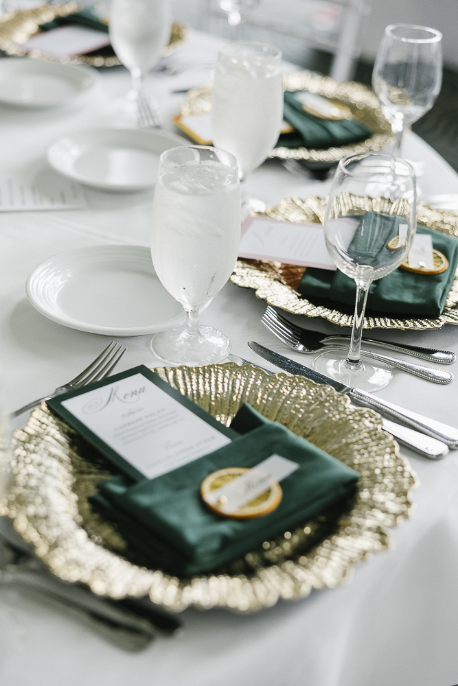 Elegant table setting with plates, glasses, and a menu on a gold-rimmed charger plate, with a napkin and spoon.