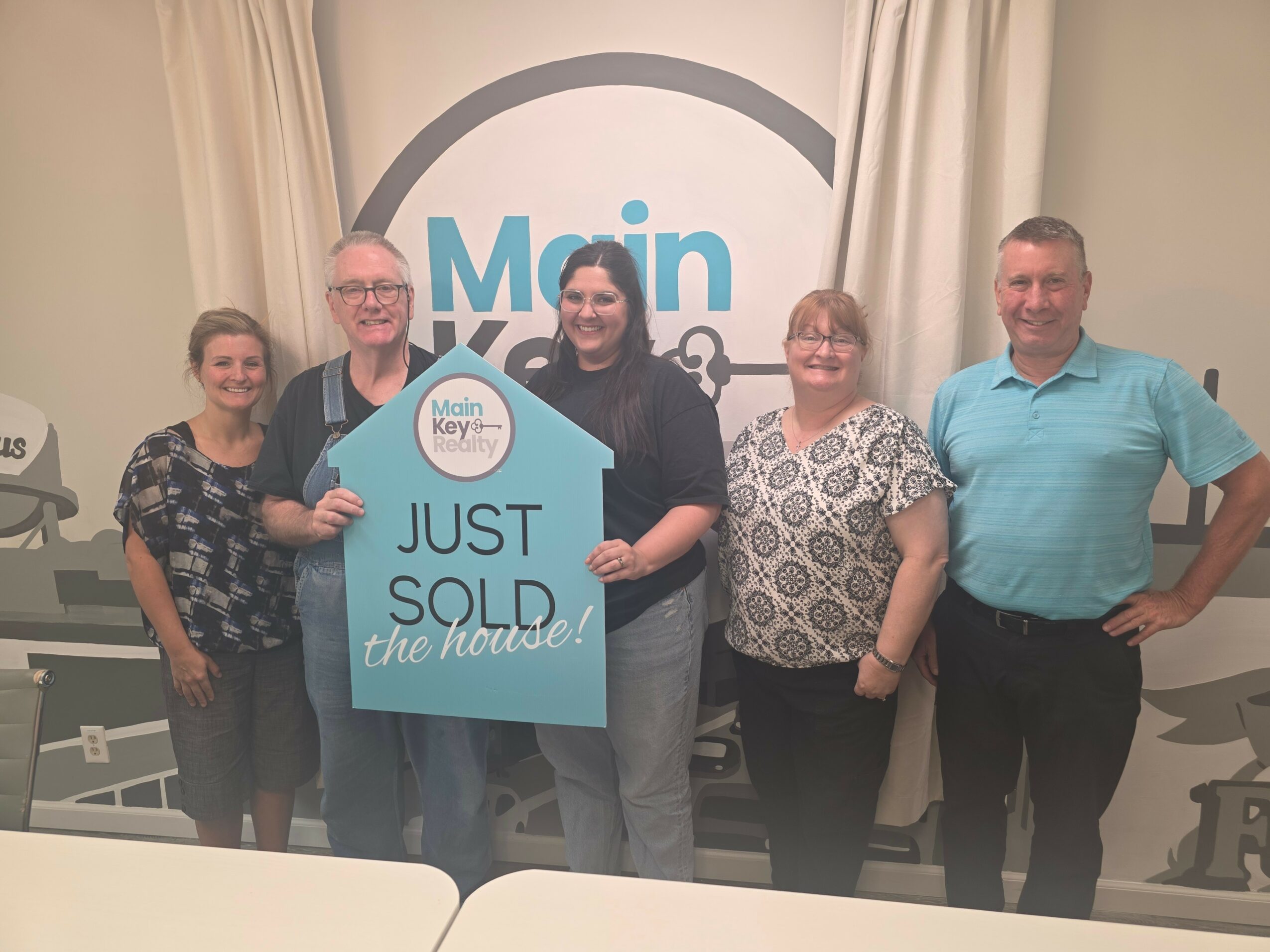 Group of five people standing indoors, holding a sign that says 