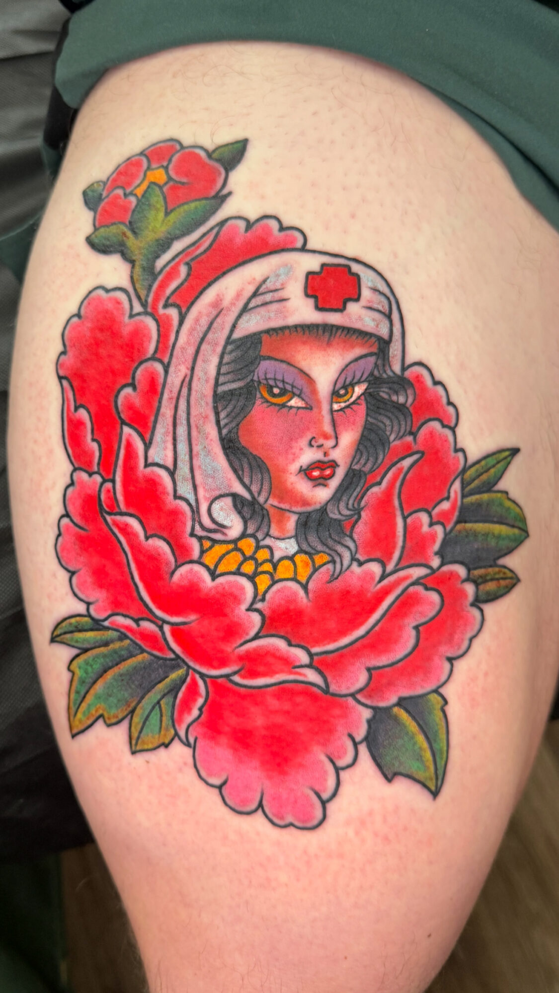 Tattoo of a woman with a nurse's cap surrounded by large red flowers and green leaves.