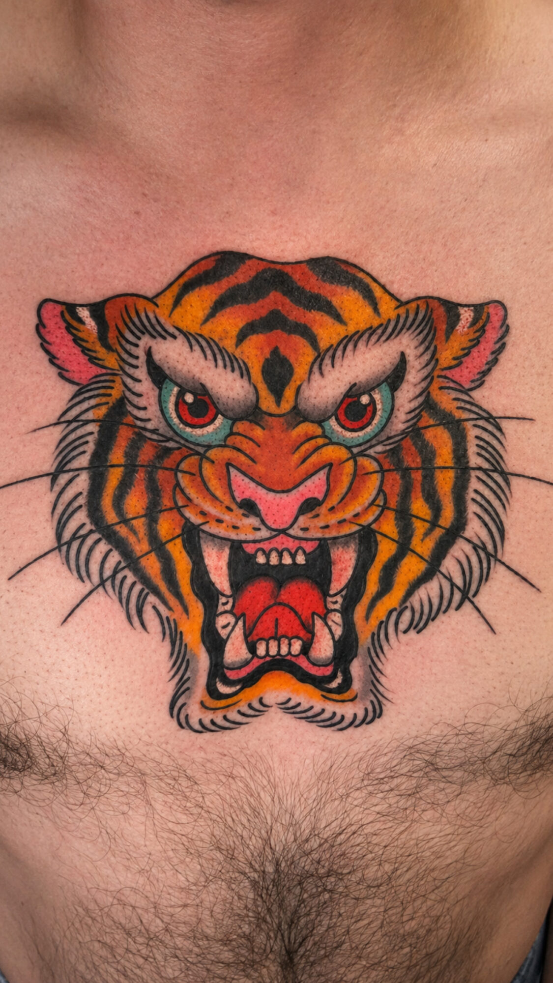 Tattoo of a fierce tiger's face with detailed orange, black, and pink colors on a person's chest.