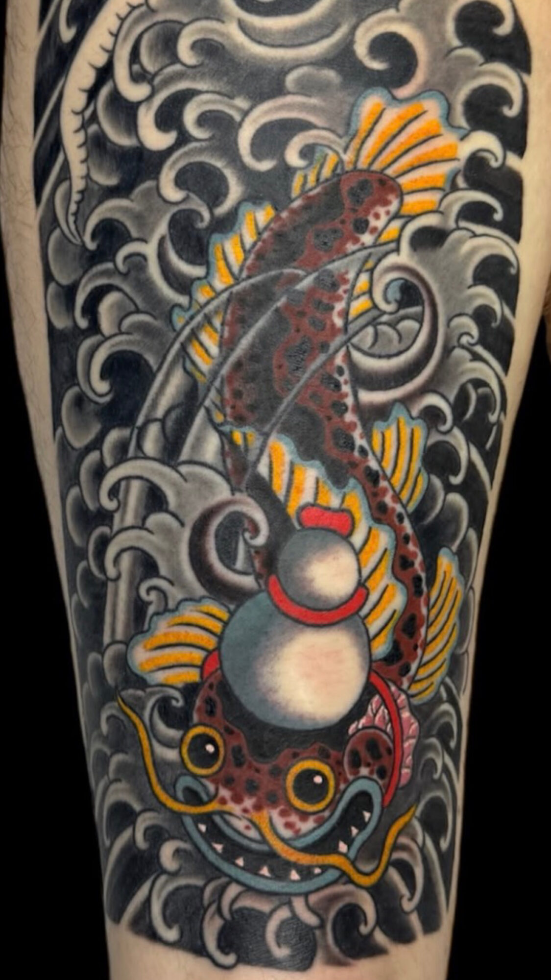 Colorful fish with yellow fins swimming among stylized waves and clouds, with a large pearl at the bottom, in traditional tattoo style.