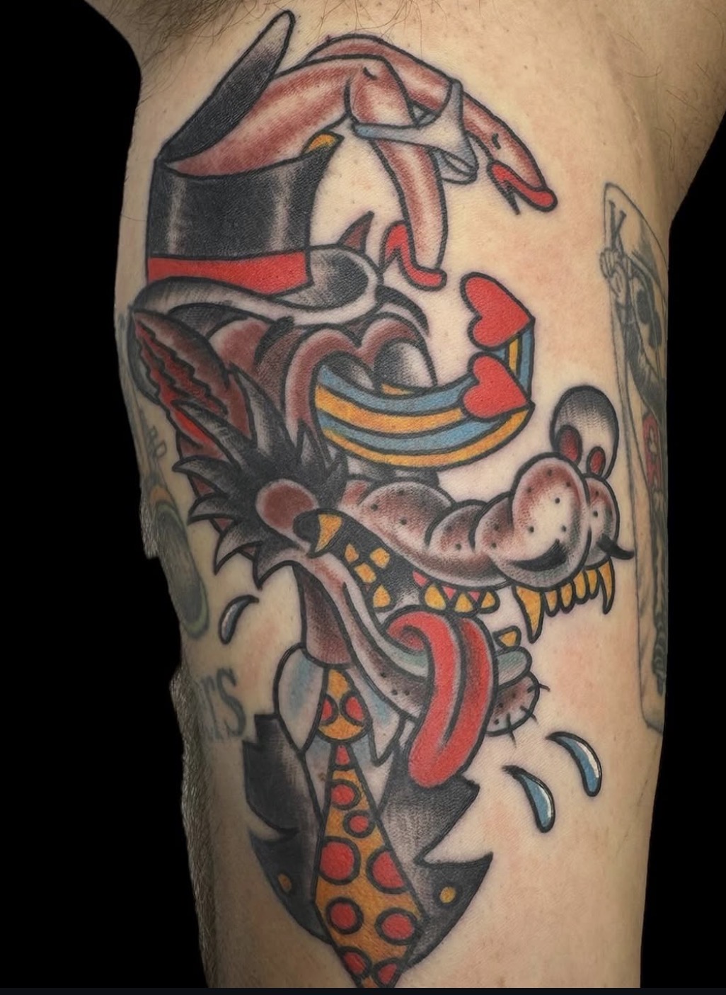 Tattoo of a dragon with a tongue, hearts, and colorful details on a person's arm.
