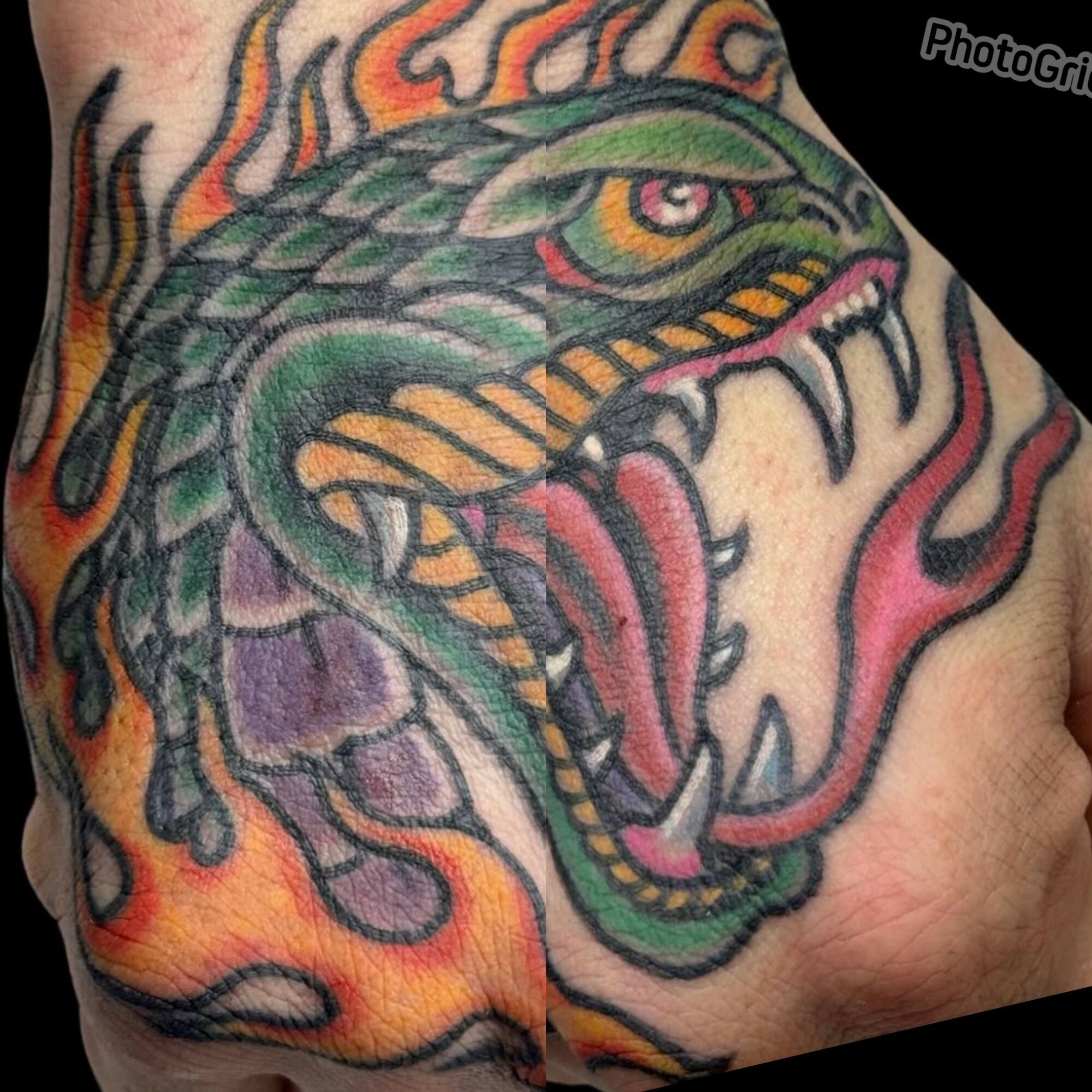 Colorful dragon tattoo with flames, detailed scales, and an open mouth showing sharp teeth on a person's shoulder.
