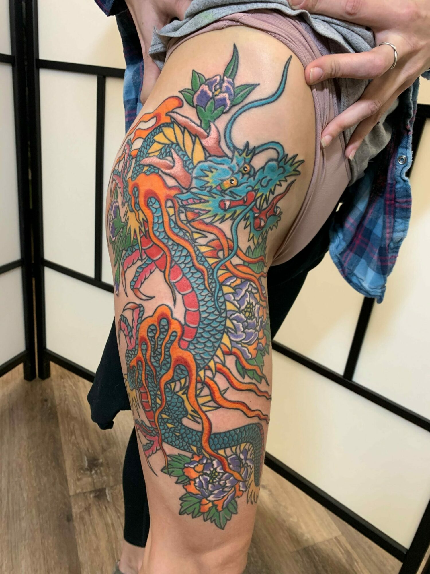Colorful dragon tattoo on person's arm with detailed scales, claws, and flames, extending from shoulder to forearm.
