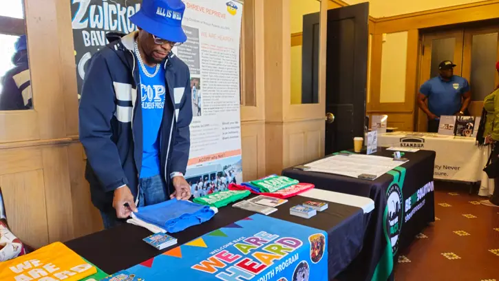 Person wearing a blue hat and jacket looking at items on a table with colorful banners, in an indoor setting.