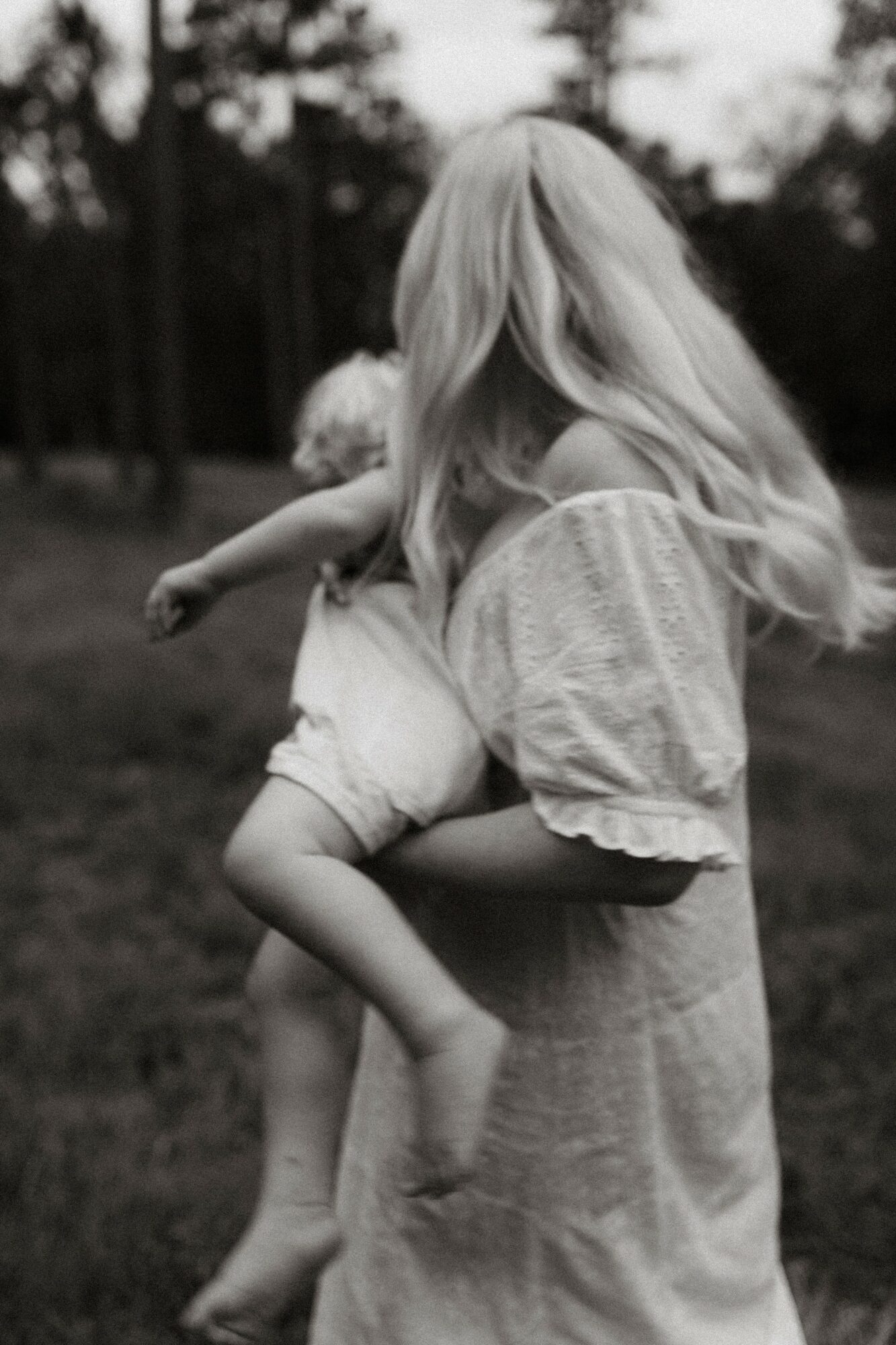 Woman holding a child outdoors, both with long hair, in a natural setting, black and white photo.