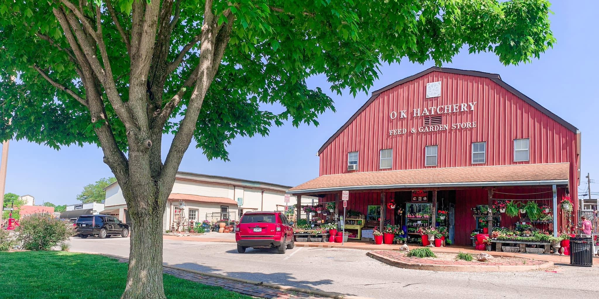 Red barn-style building with a sign, surrounded by trees and parking lot, under a clear blue sky.