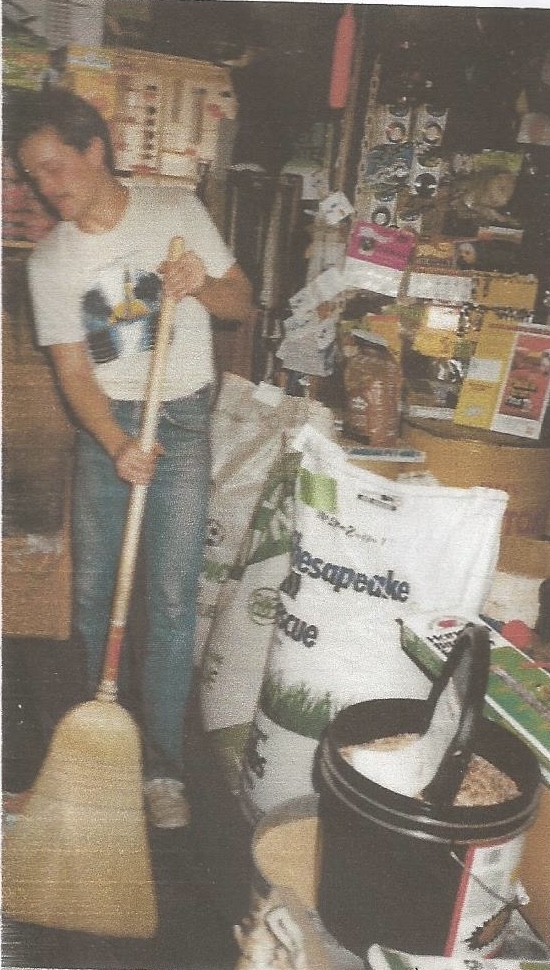 Person cleaning store floor with broom, shelves and products in background.