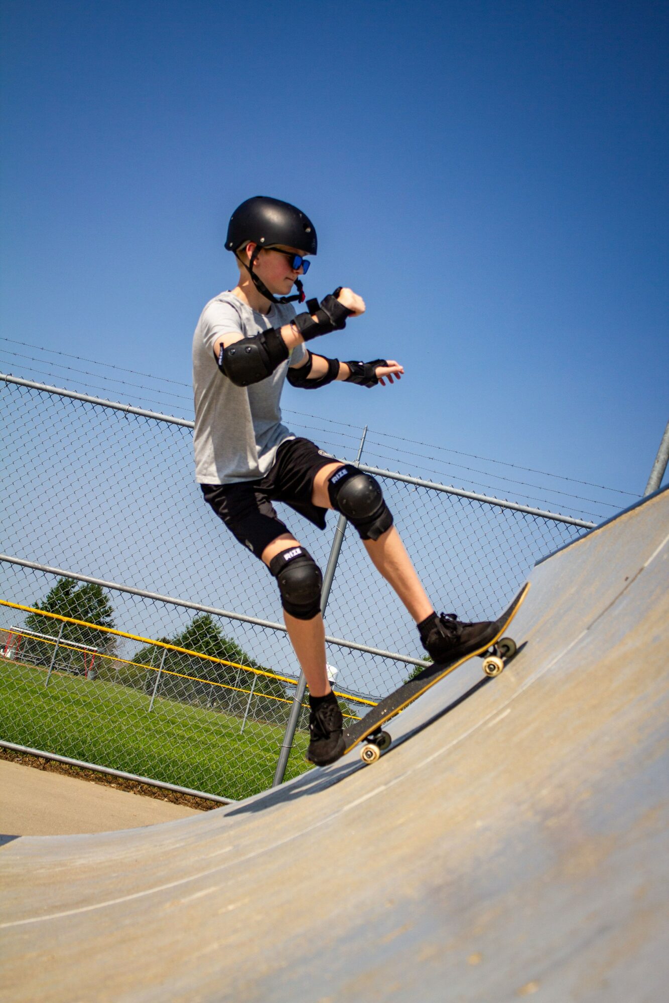 Person wearing helmet and protective gear skateboarding on a ramp outdoors under a clear blue sky.
