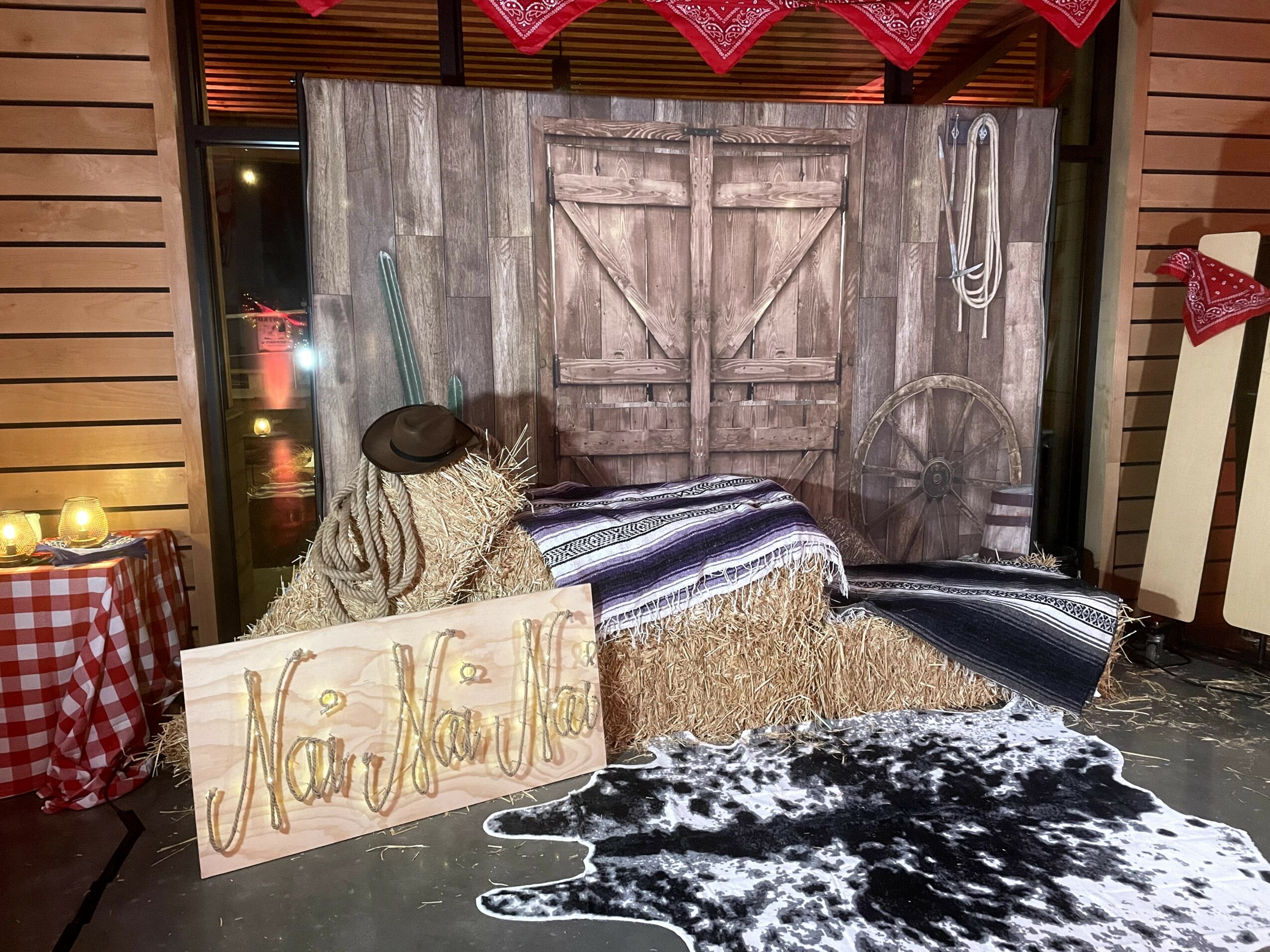 Rustic wooden door with hay bales, a cowhide rug, and a handmade sign reading 'Merry Christmas' in front of a festive backdrop.