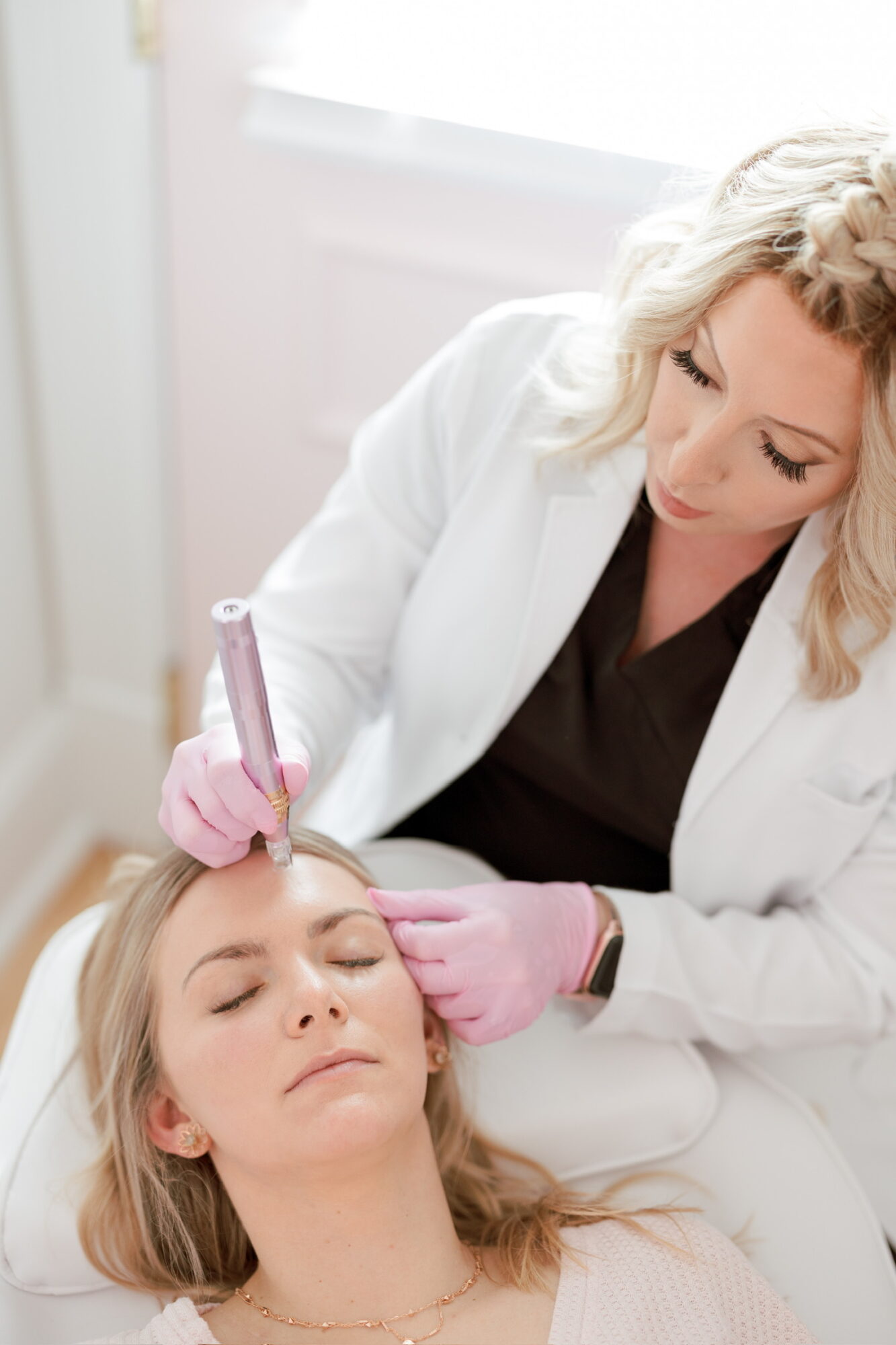 A woman with blonde hair receives a cosmetic treatment from a professional in a clinical setting.