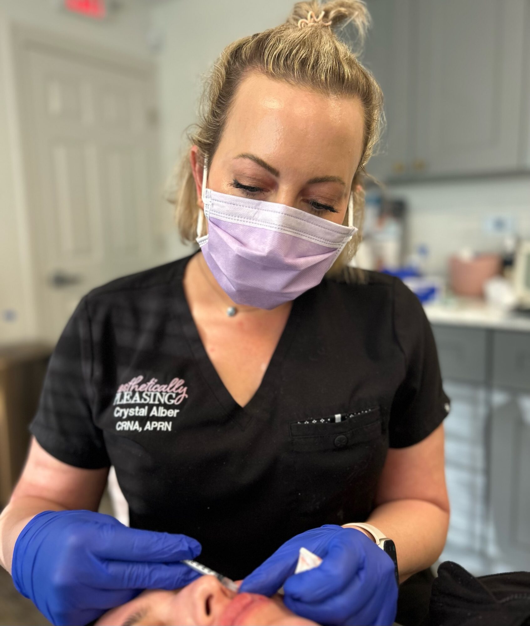 Woman wearing a face mask and gloves, preparing a medical procedure in a clinical setting.