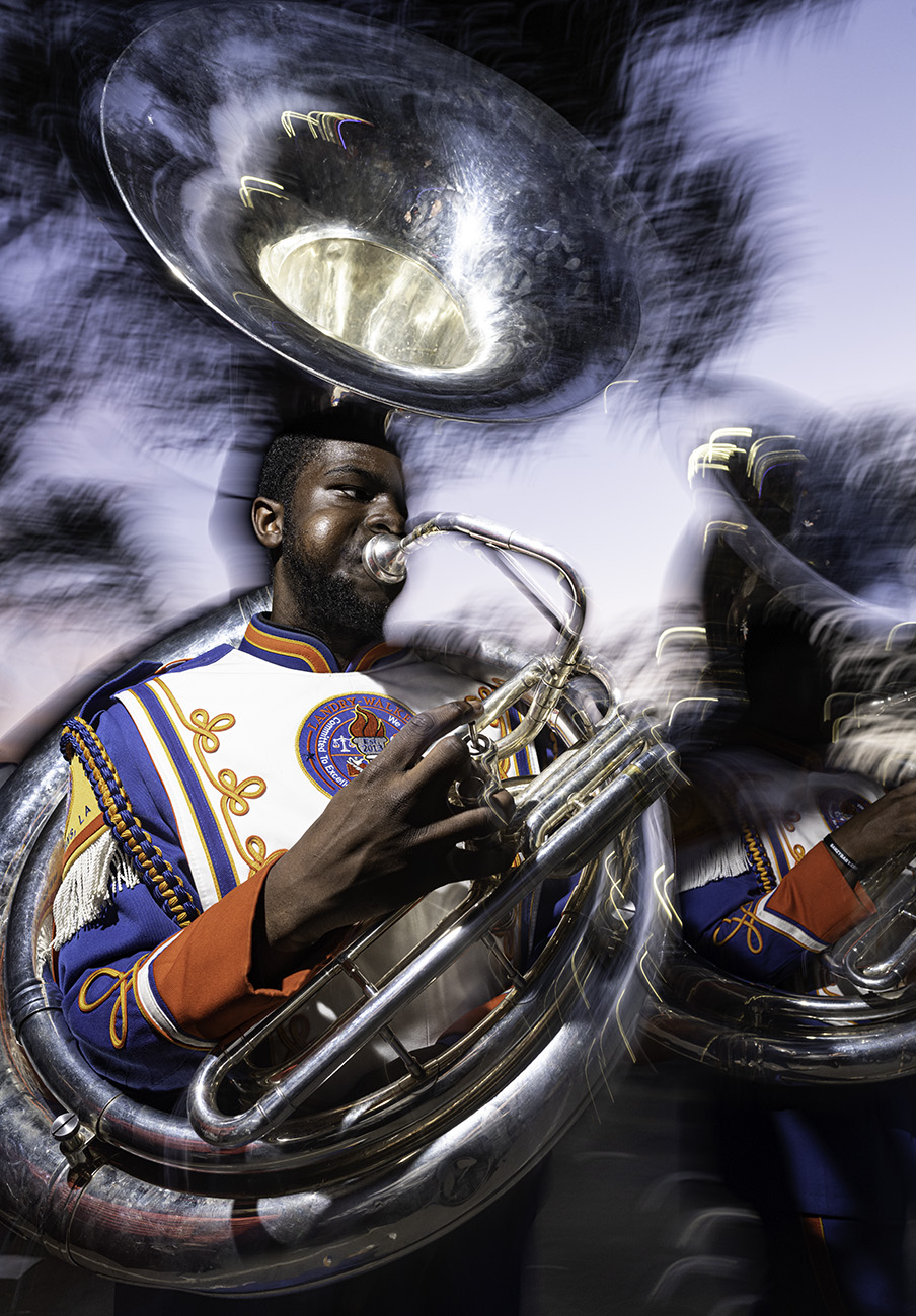 Musician playing a brass instrument with smoke around him, wearing a colorful uniform, in a performance setting.