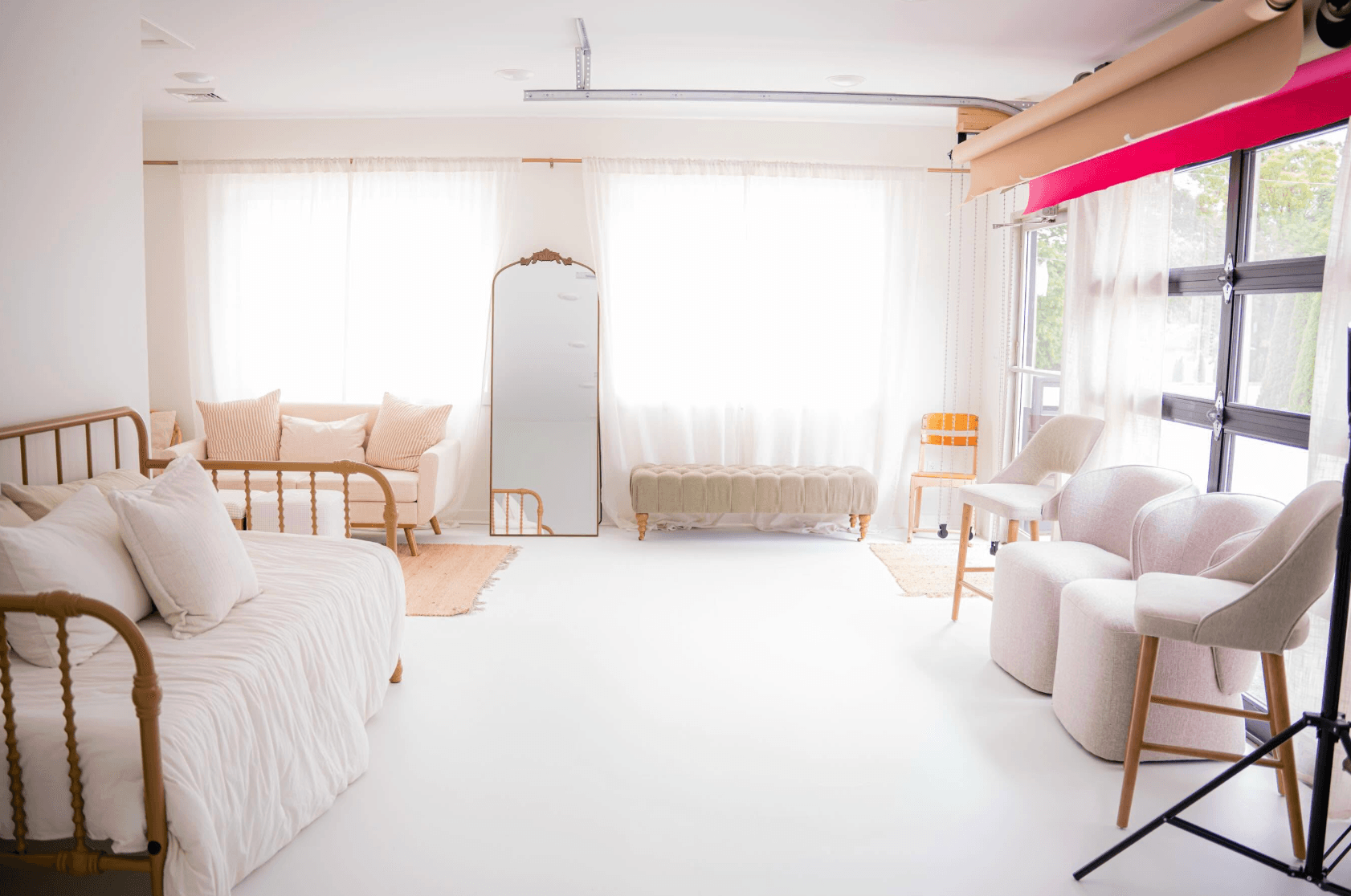 Bright, airy room with white walls, large windows, and minimal furniture including a bed, chairs, and a mirror.
