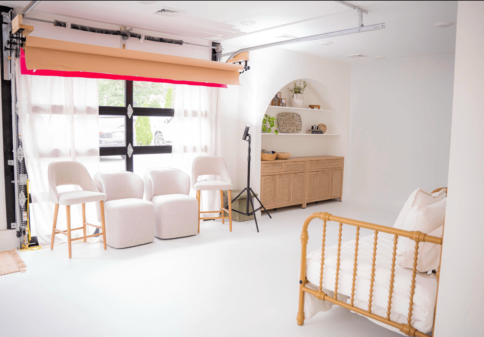 Bright room with white furniture, large window with curtains, wooden cabinet, and a crib, illuminated by natural light.