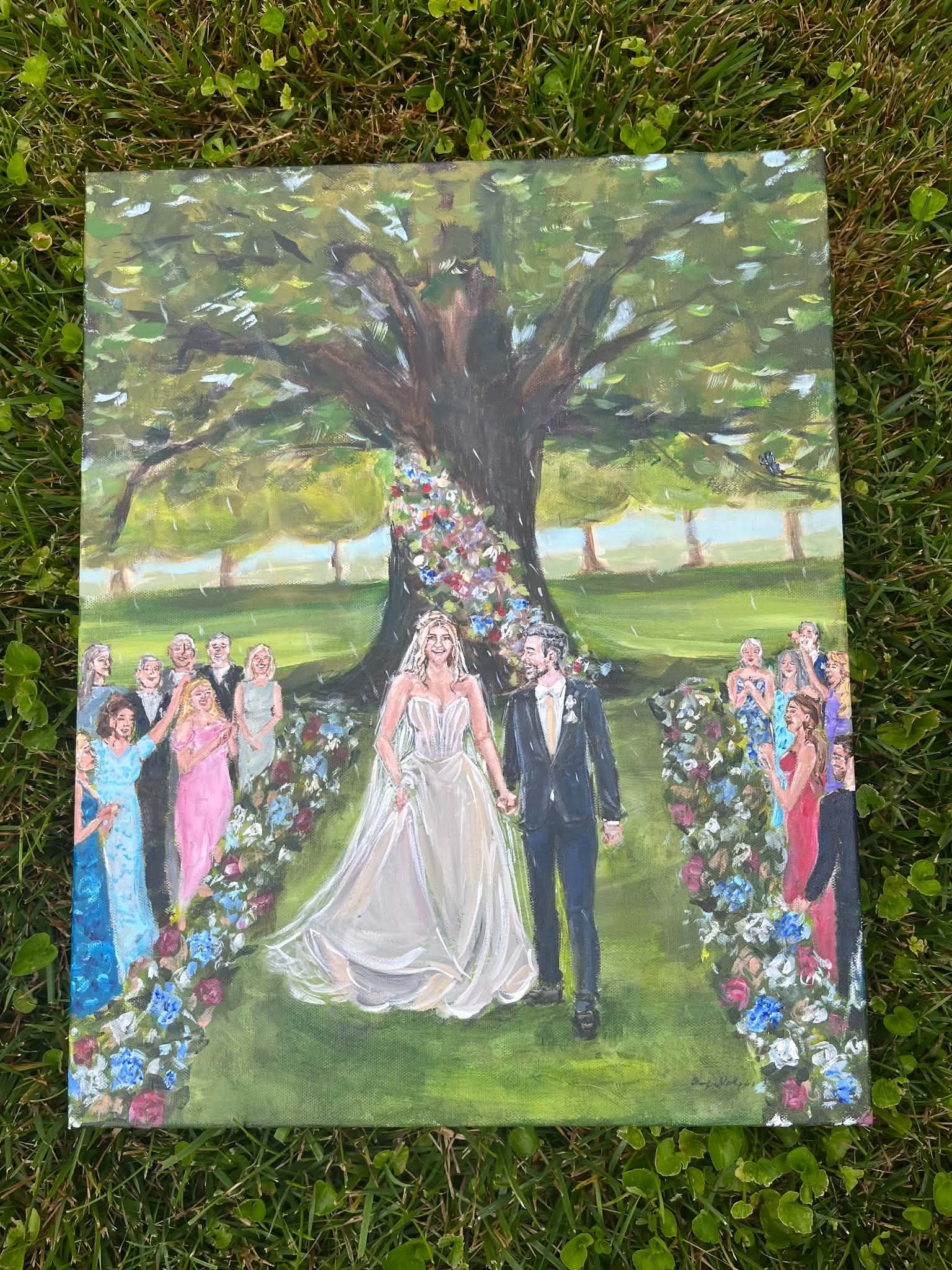 Wedding couple walking under a large tree with colorful flowers and guests on both sides in a garden.