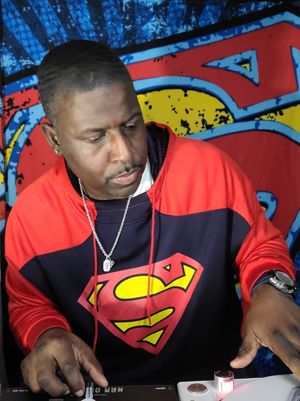 Man wearing a Superman hoodie, listening to earphones, looking down, with a colorful graffiti background.