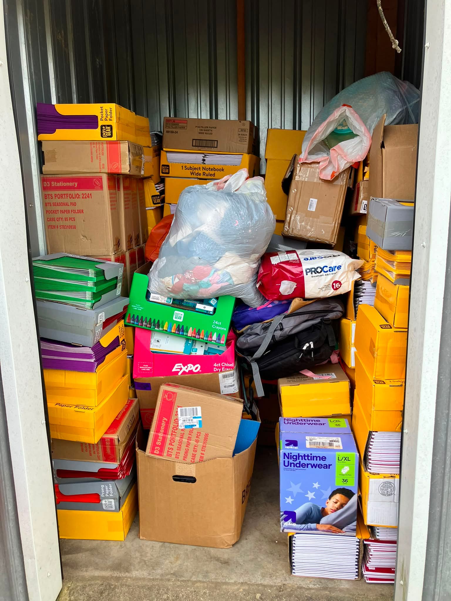 Storage closet filled with stacked boxes, bags, and miscellaneous items, including clothing and packaging materials.