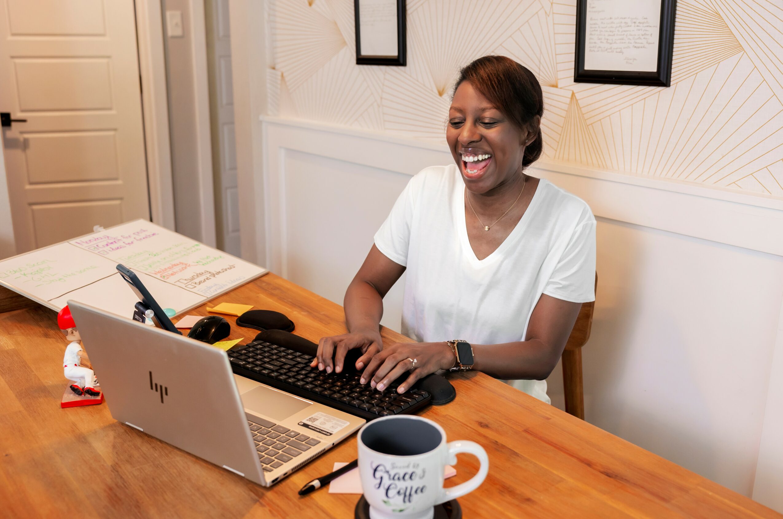 Woman smiling at a laptop in an office, with a mug and papers on the desk.