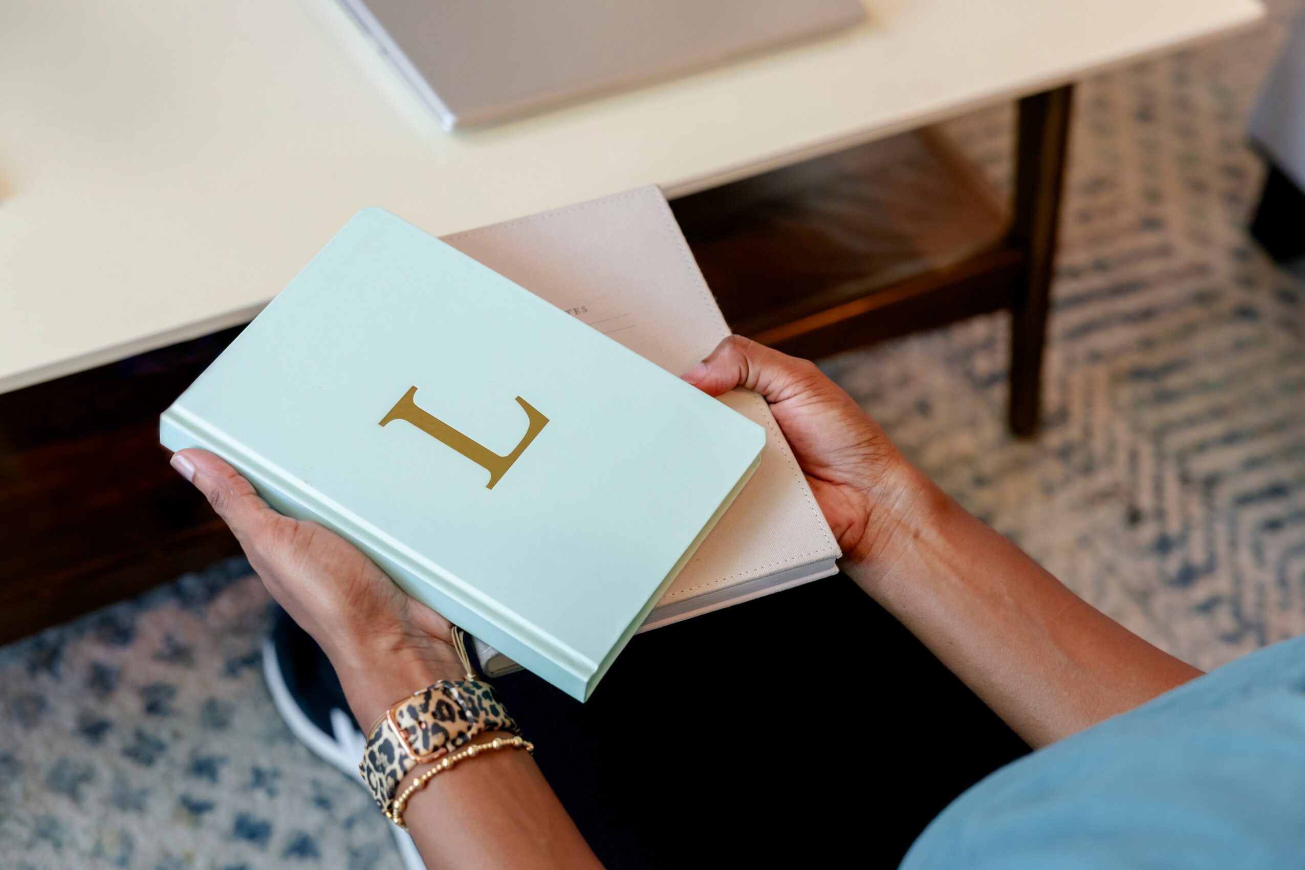 Person holding a light blue book with a large gold letter 'L' on the cover, sitting at a table.