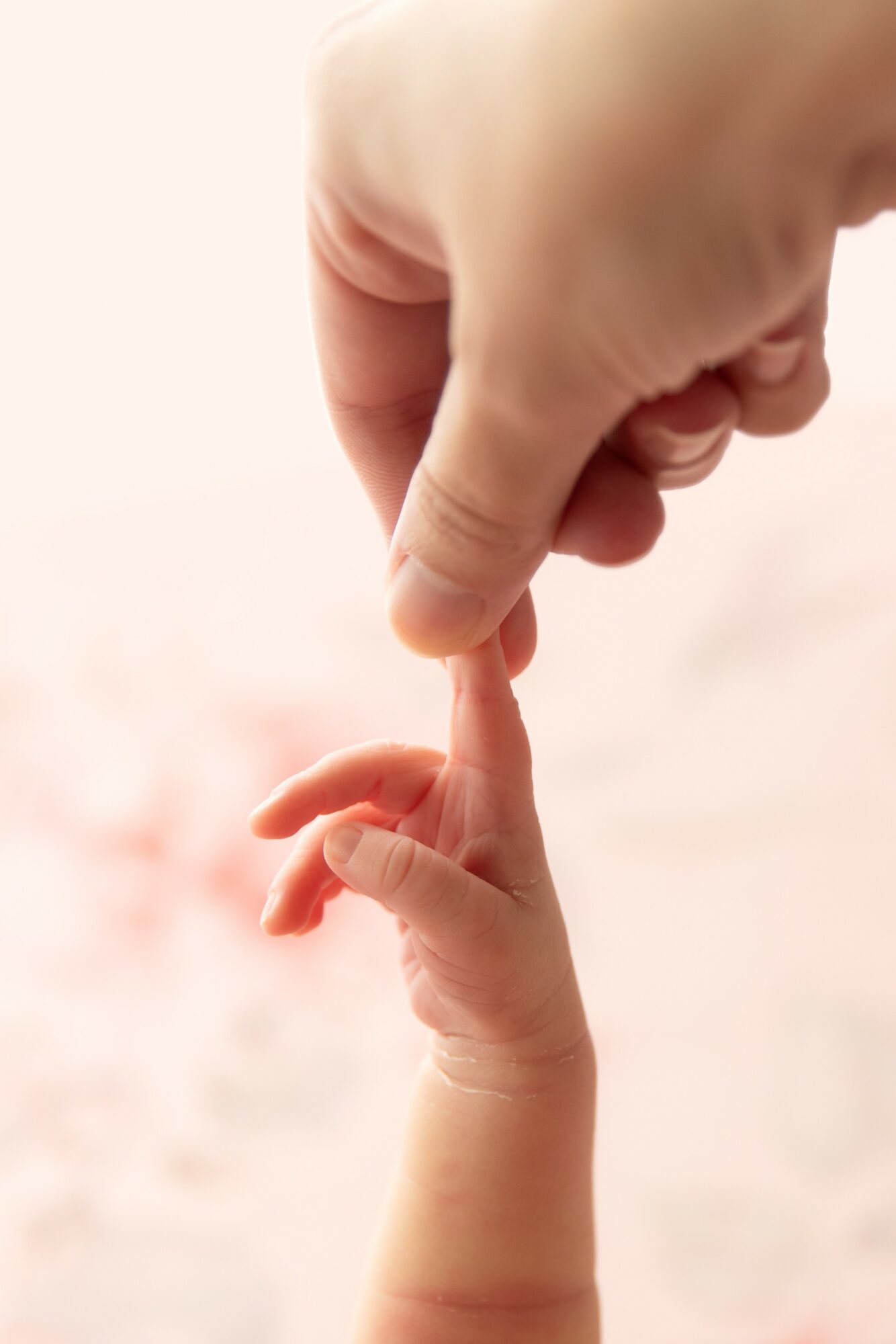 Adult hand gently holding a baby's finger, with a soft background.