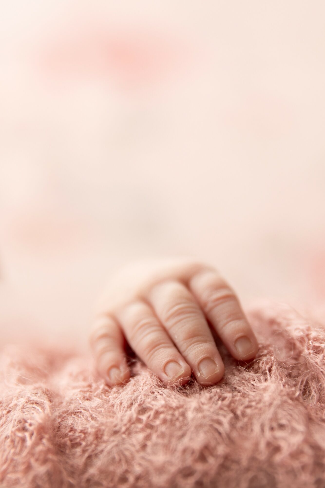 Close-up of a small hand resting on a soft, pink textured surface.