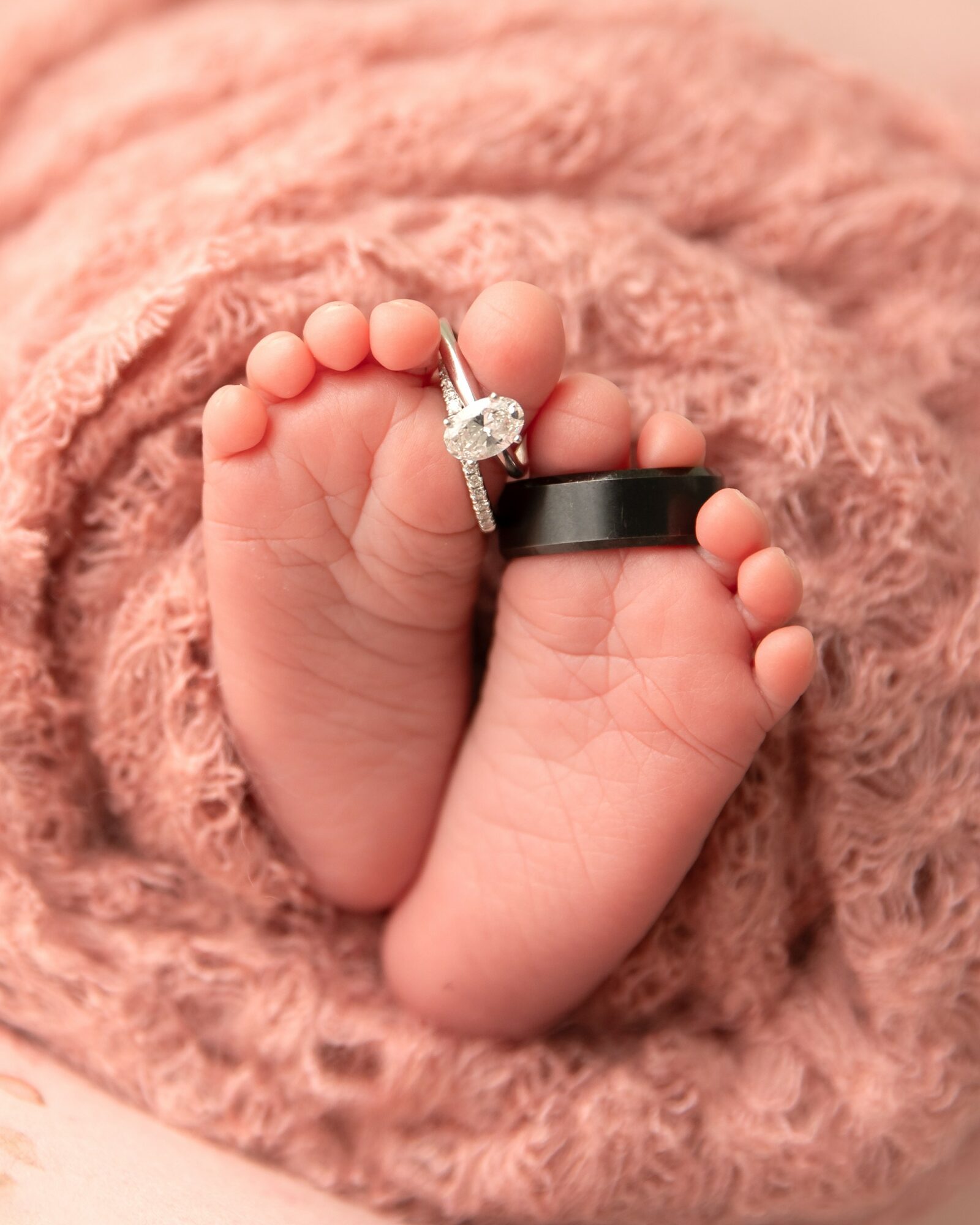 Close-up of tiny baby feet with a ring and a black band, wrapped in soft pink fabric.