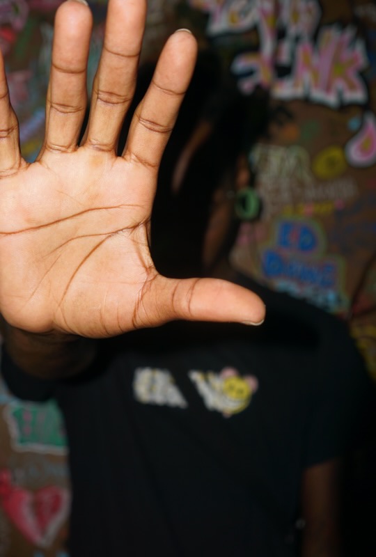 Hand with fingers spread open, palm facing the camera, against a colorful background.