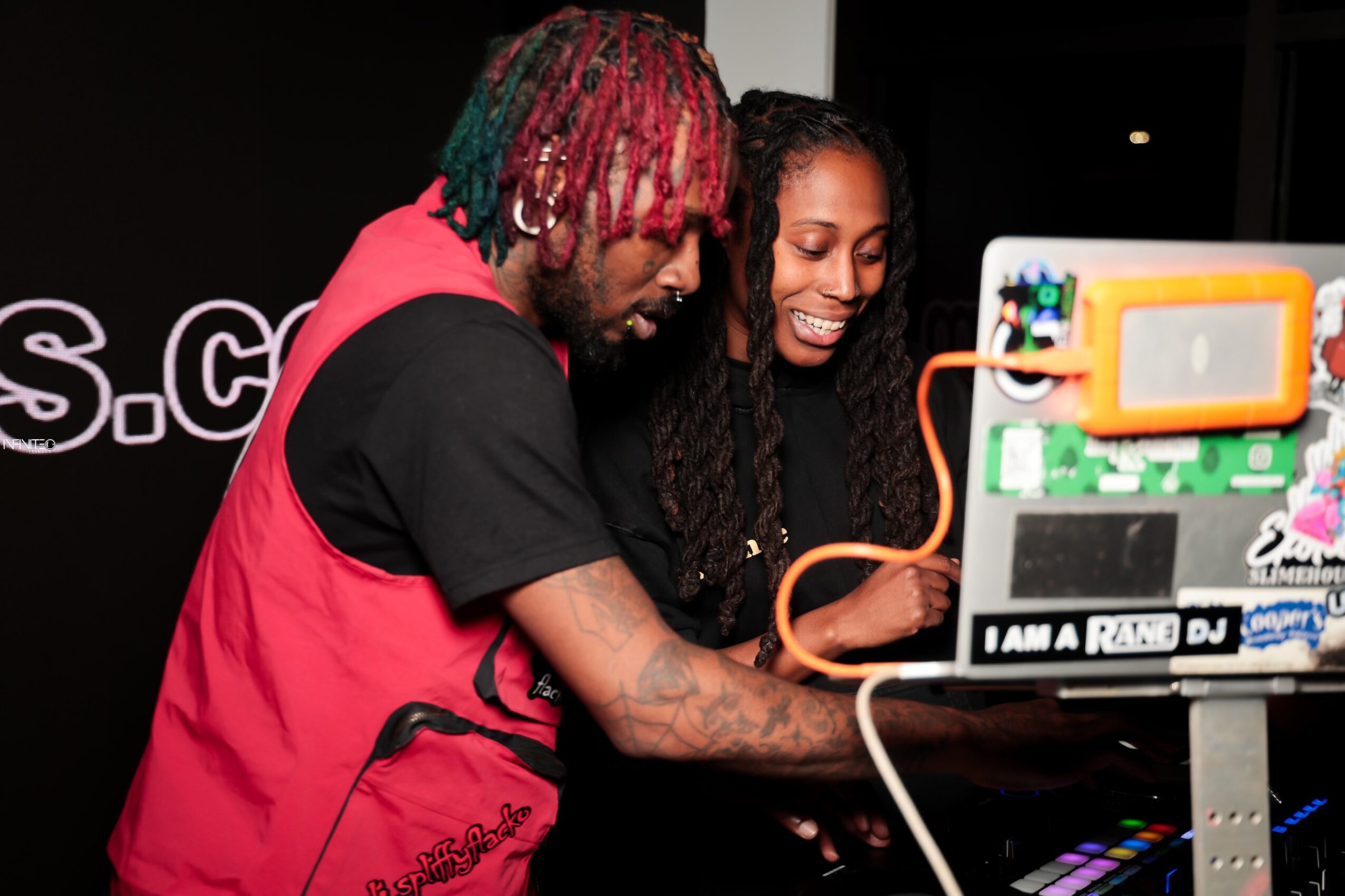 Two people look at a screen with colorful equipment, smiling and engaging with the device in a dark room.