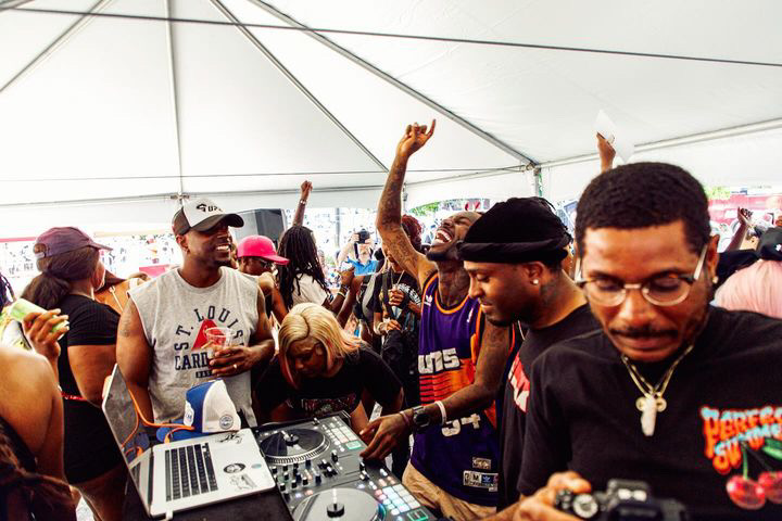 Group of people dancing and socializing under a tent at an outdoor event, with DJ equipment visible.