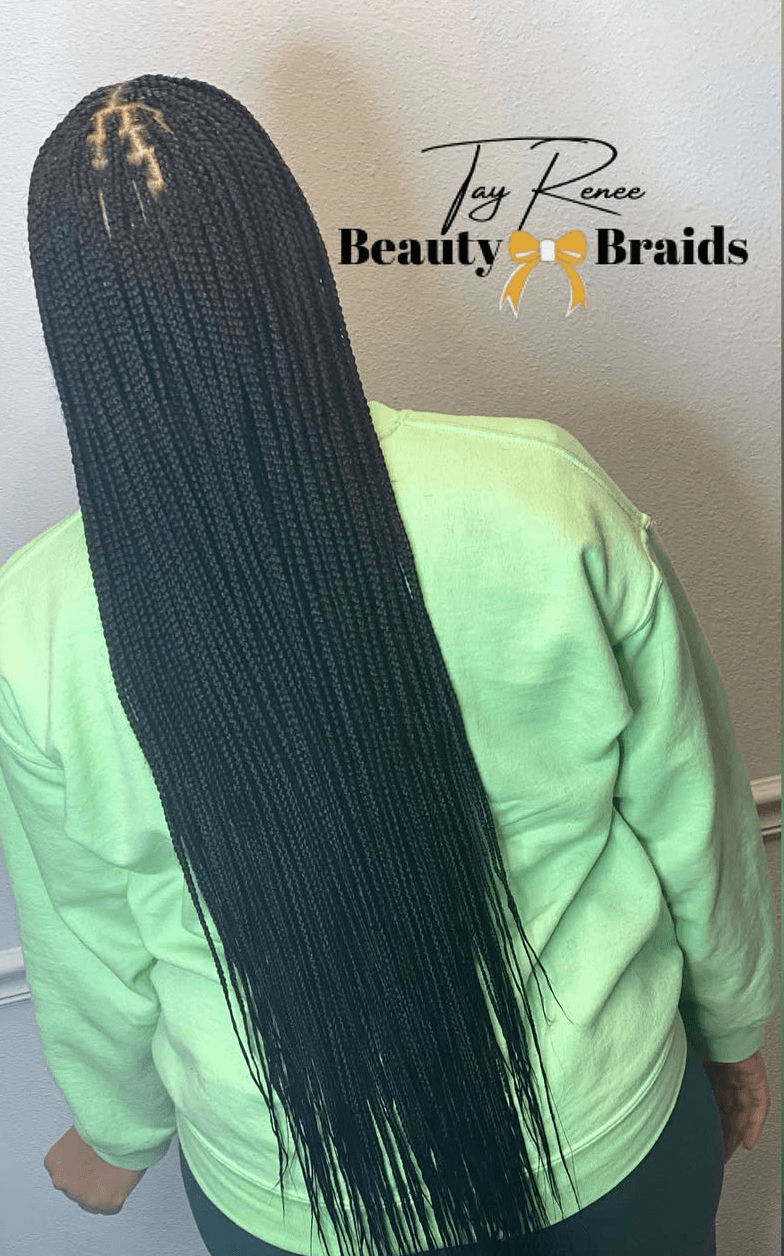 Back view of a person with long, black, braided hair wearing a light green sweatshirt, standing against a plain wall.