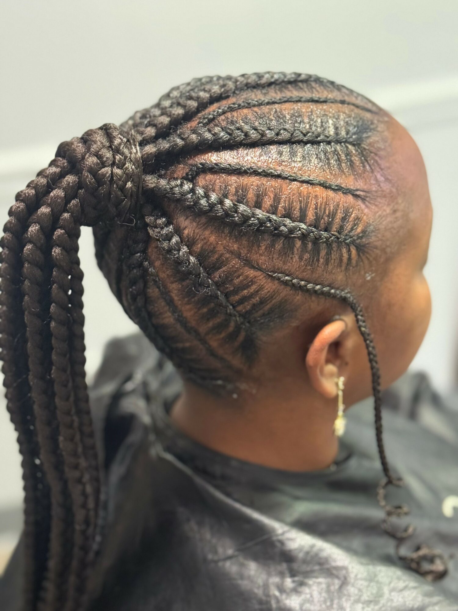 Side view of a person with braided hairstyle, including cornrows and long braids, wearing earrings and a black top.