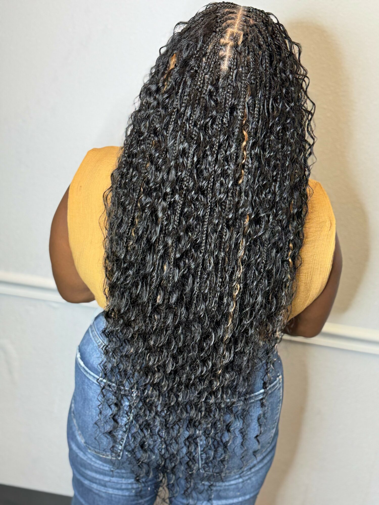Back view of a person with long, curly black hair wearing a yellow top and blue jeans.